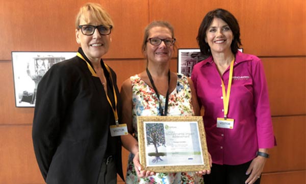 Three women with an award stand in front of a framed poster